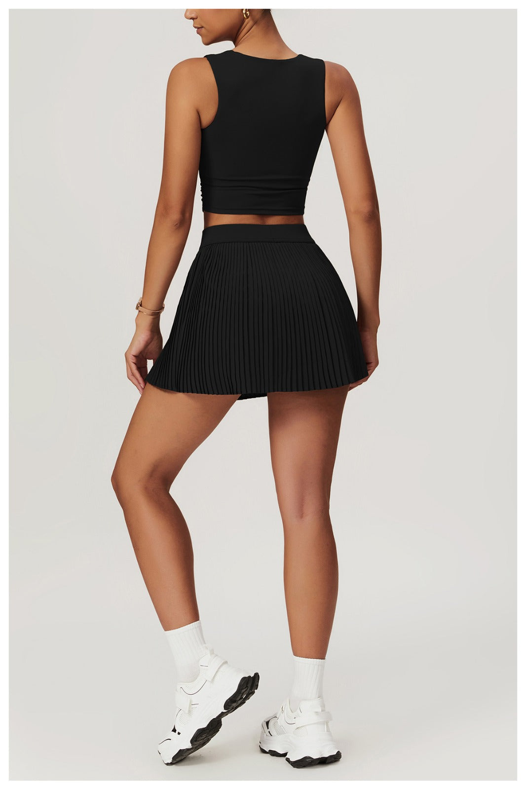 Person wearing a black sleeveless top and pleated skort with white sneakers on a light gray background