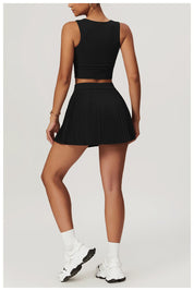 Person wearing a black sleeveless top and pleated skort with white sneakers on a light gray background