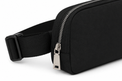 A close-up of a black nylon waist bag with an adjustable black webbing strap and silver metal zipper hardware, shown on a white background.
