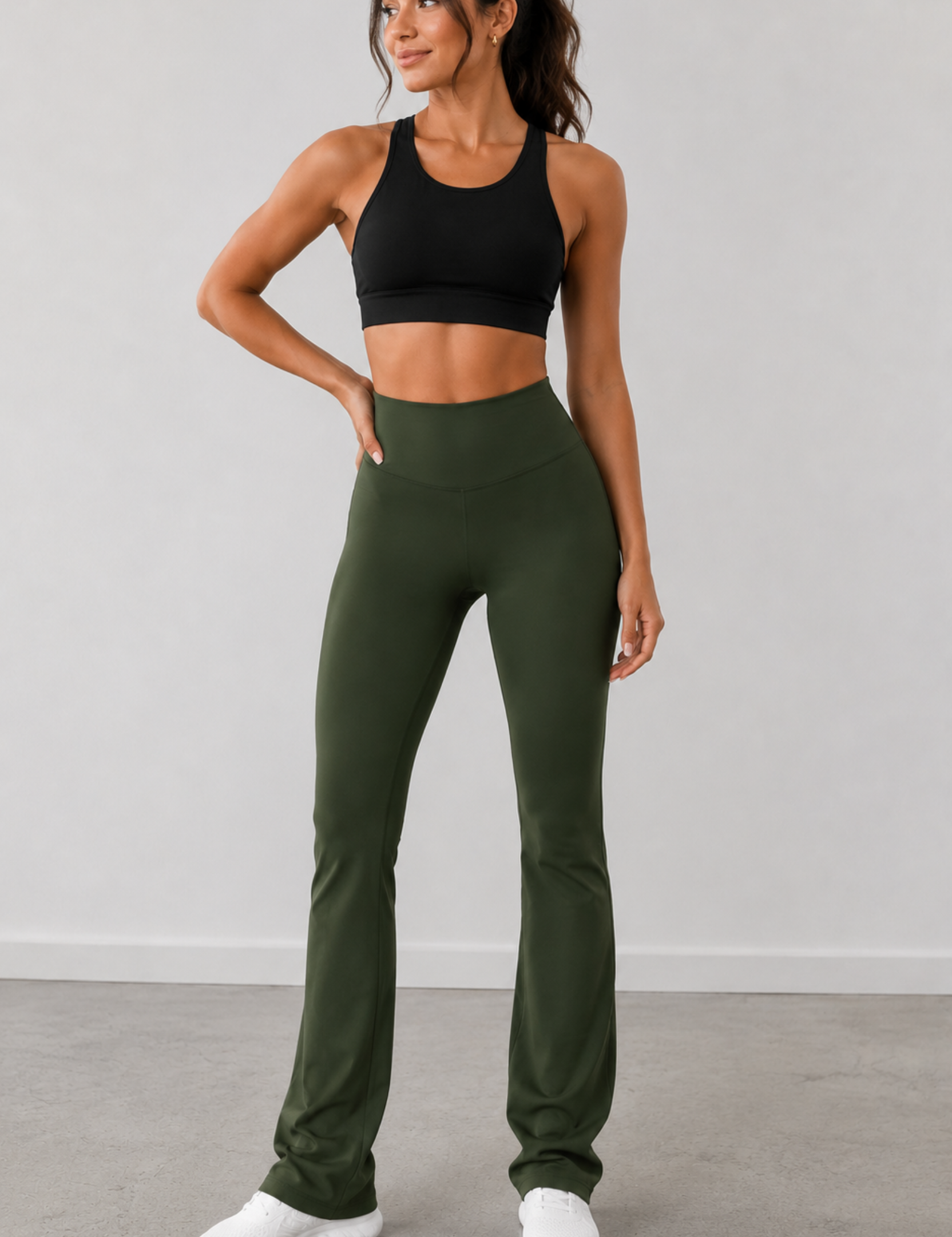 Woman wearing a black sports bra and green leggings against a gray background