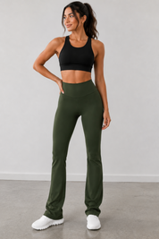 Woman wearing a black sports bra and green leggings against a gray background