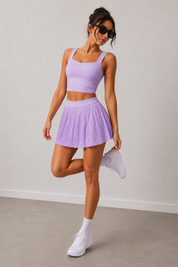 Woman wearing a purple athletic outfit with a skirt and top, standing against a plain background.
