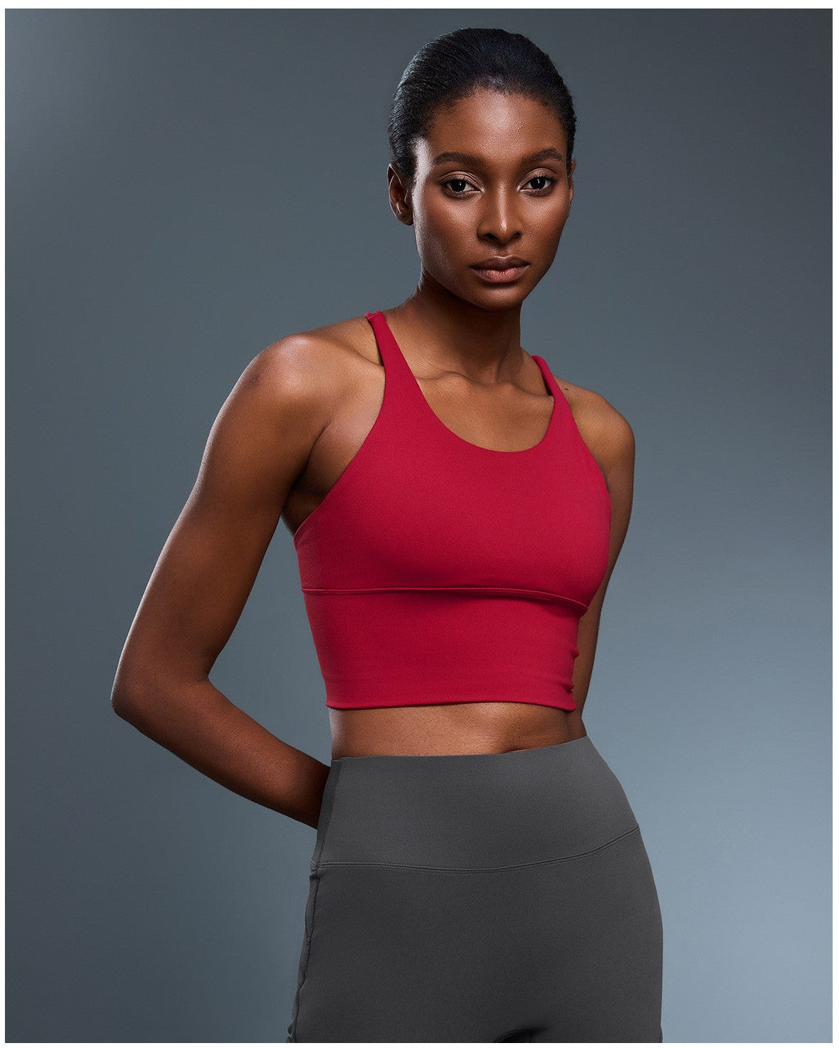 Woman wearing a red sports bra and gray leggings on a gray background