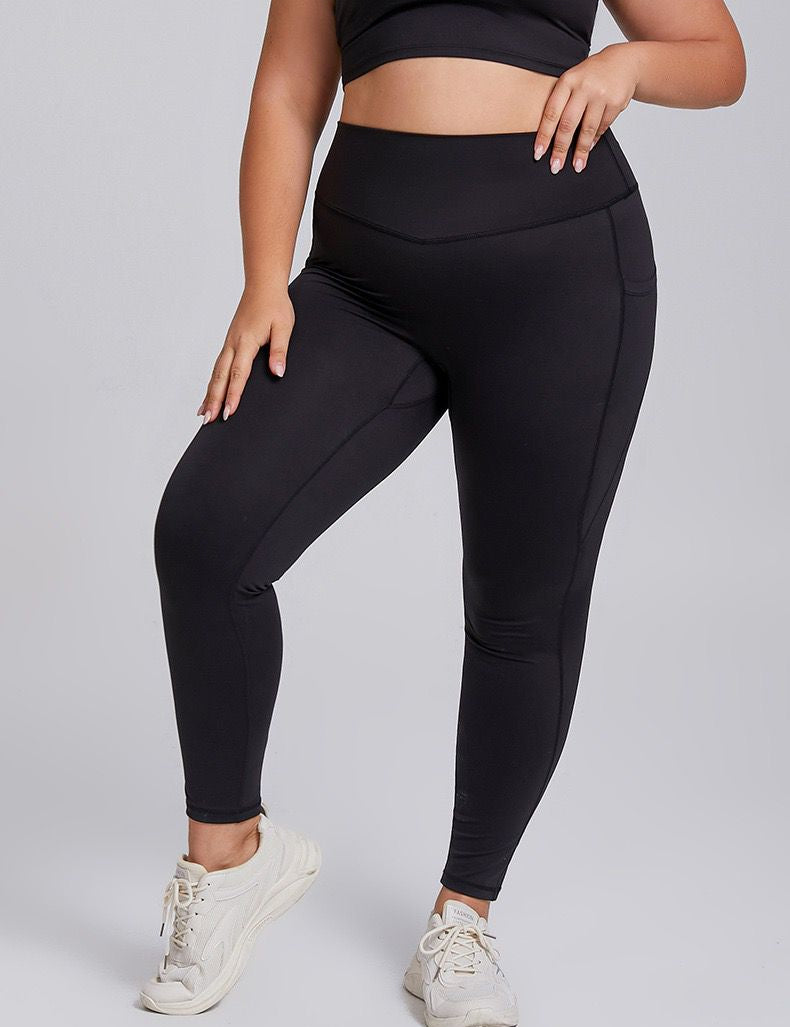 A woman wearing a high-waisted black pair of leggings with side pockets, paired with a sports bra and white sneakers, standing in a pose.