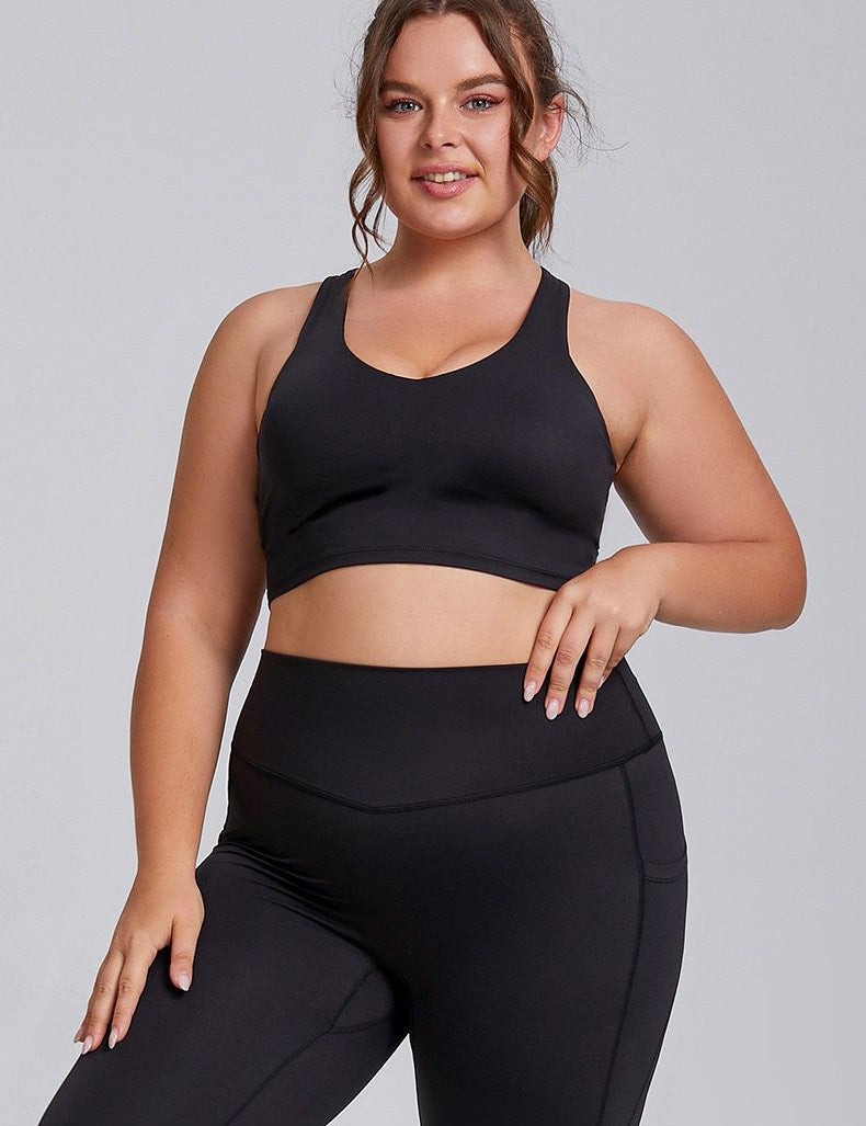 A woman wearing a black Sports Bra and matching leggings, standing and posing.